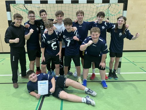 Die Handball-Mannschaft der Jungen ist zum Gruppenfoto vor dem Tor aufgestellt und zeigt die Urkunde.