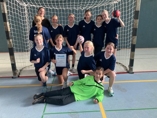Die Handball-Mannschaft der Mädchen steht vor dem Tor und zeigt ihre Urkunde.