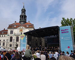 Ein Blasorchester spielt auf der Bphne auf dem Markt, viele Zuschauer stehen davor.
